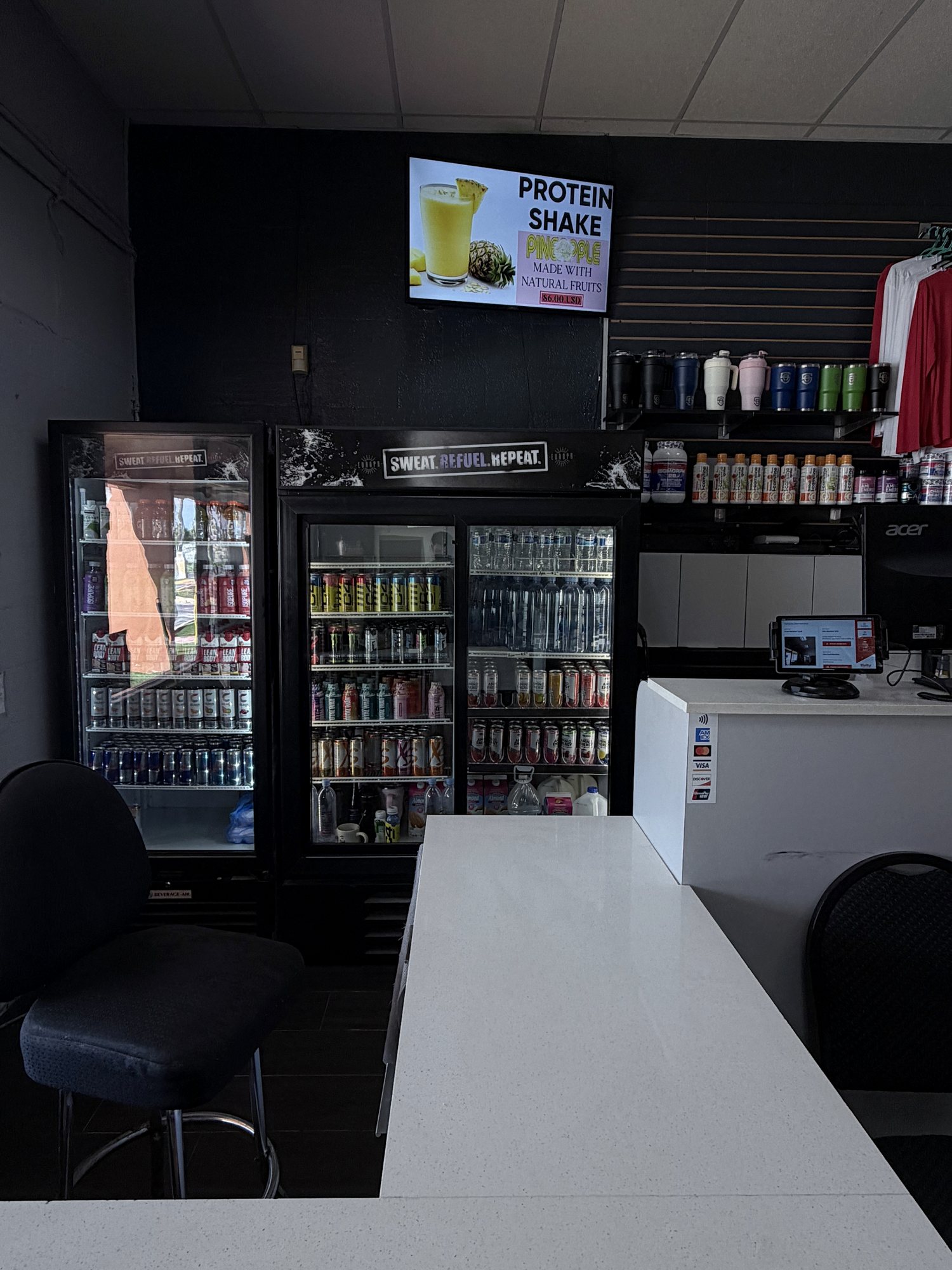 The front desk with drink fridges and a protein shake menu screen